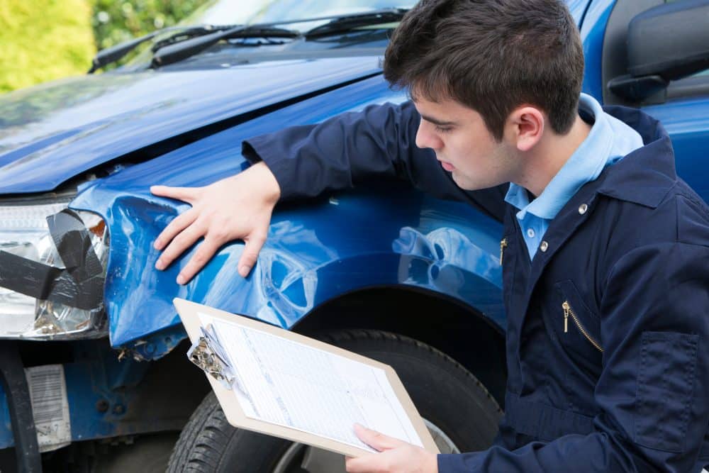 An insurance adjuster inspecting the damage to a car after an accident.
