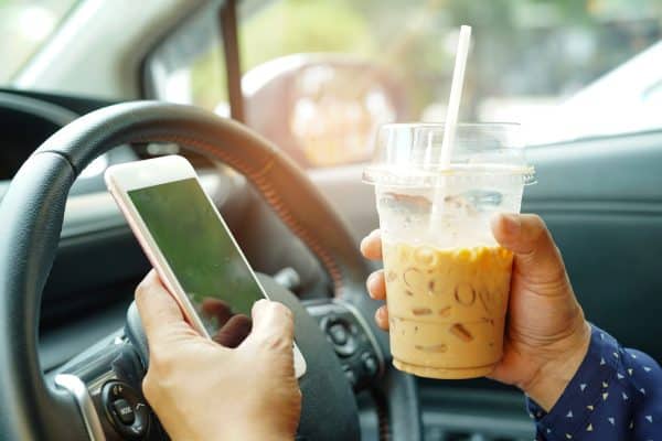 A driver holds their cell phone and a coffee instead of the wheel.