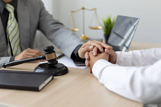 A personal injury attorney sits at their desk with one hand on top of their client’s hands.